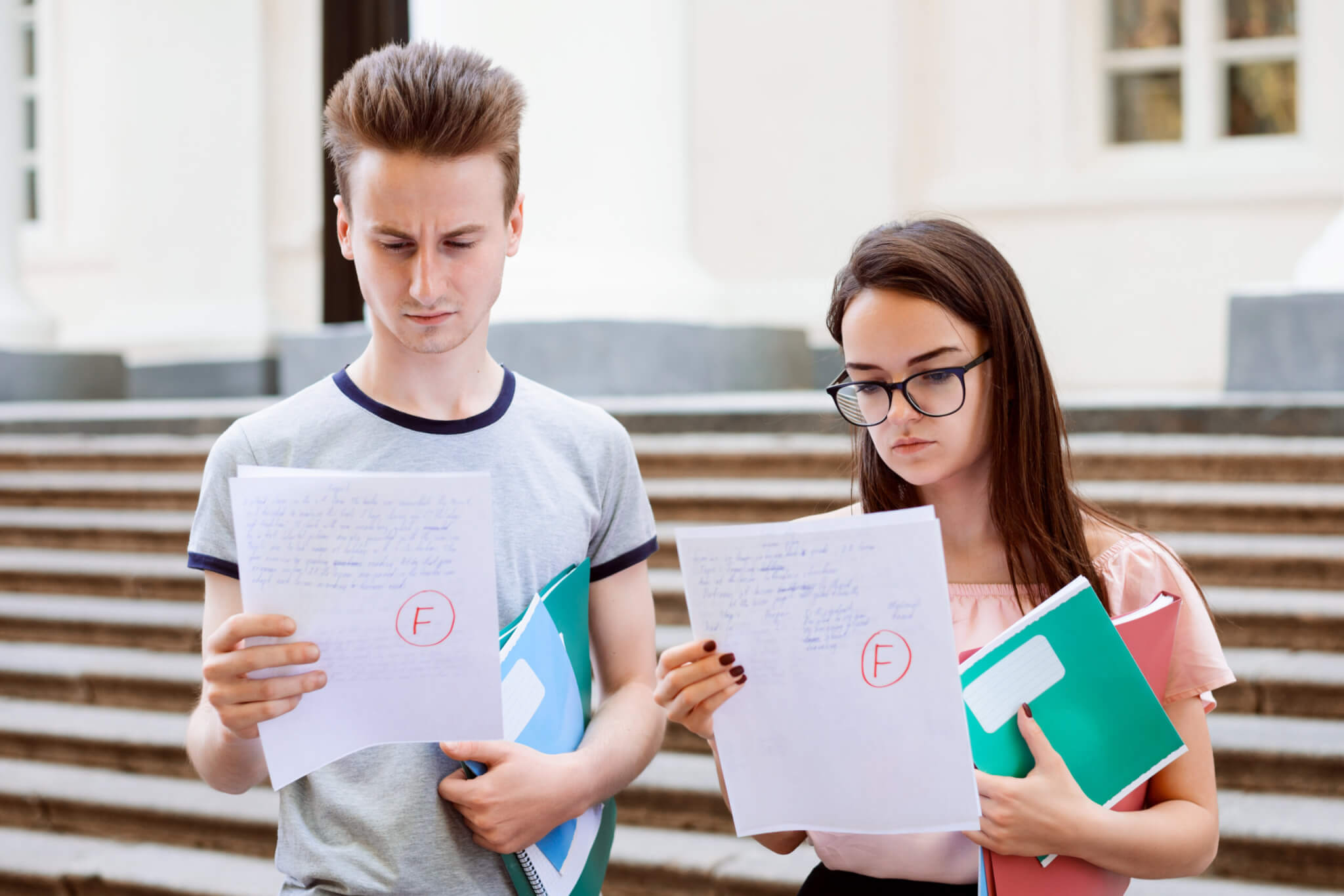 Sad students holding papers with bad results of test