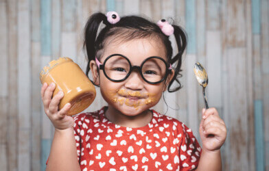 girl holding and enjoying peanut butter in jar and a spoon