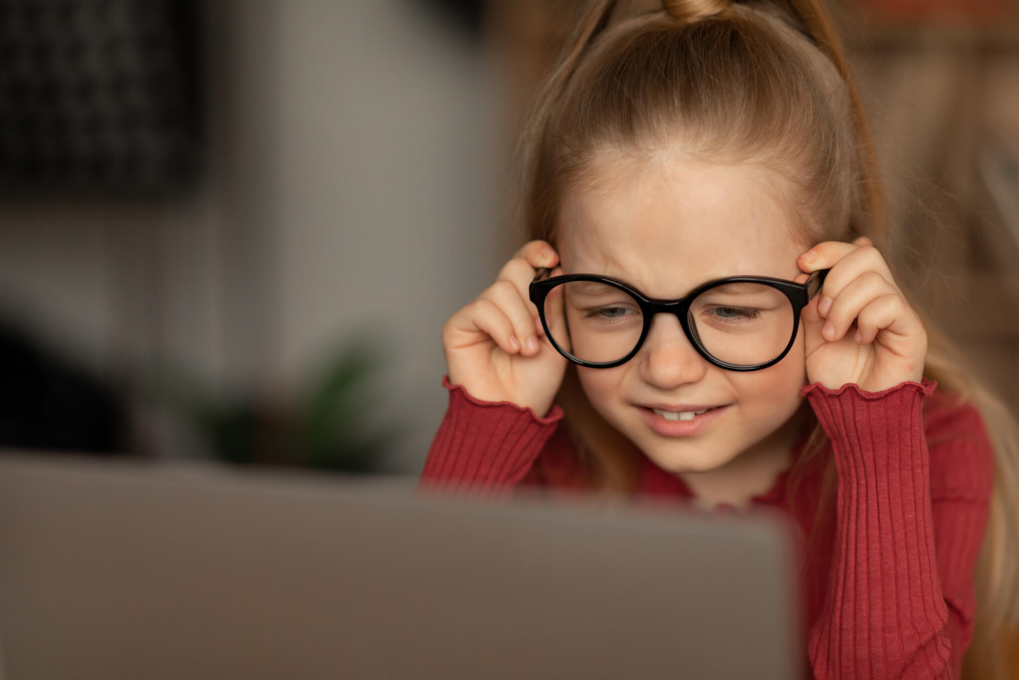 Little girl in glasses struggling with vision while looking at computer