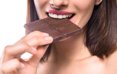 Young woman eating bar of dark chocolate.