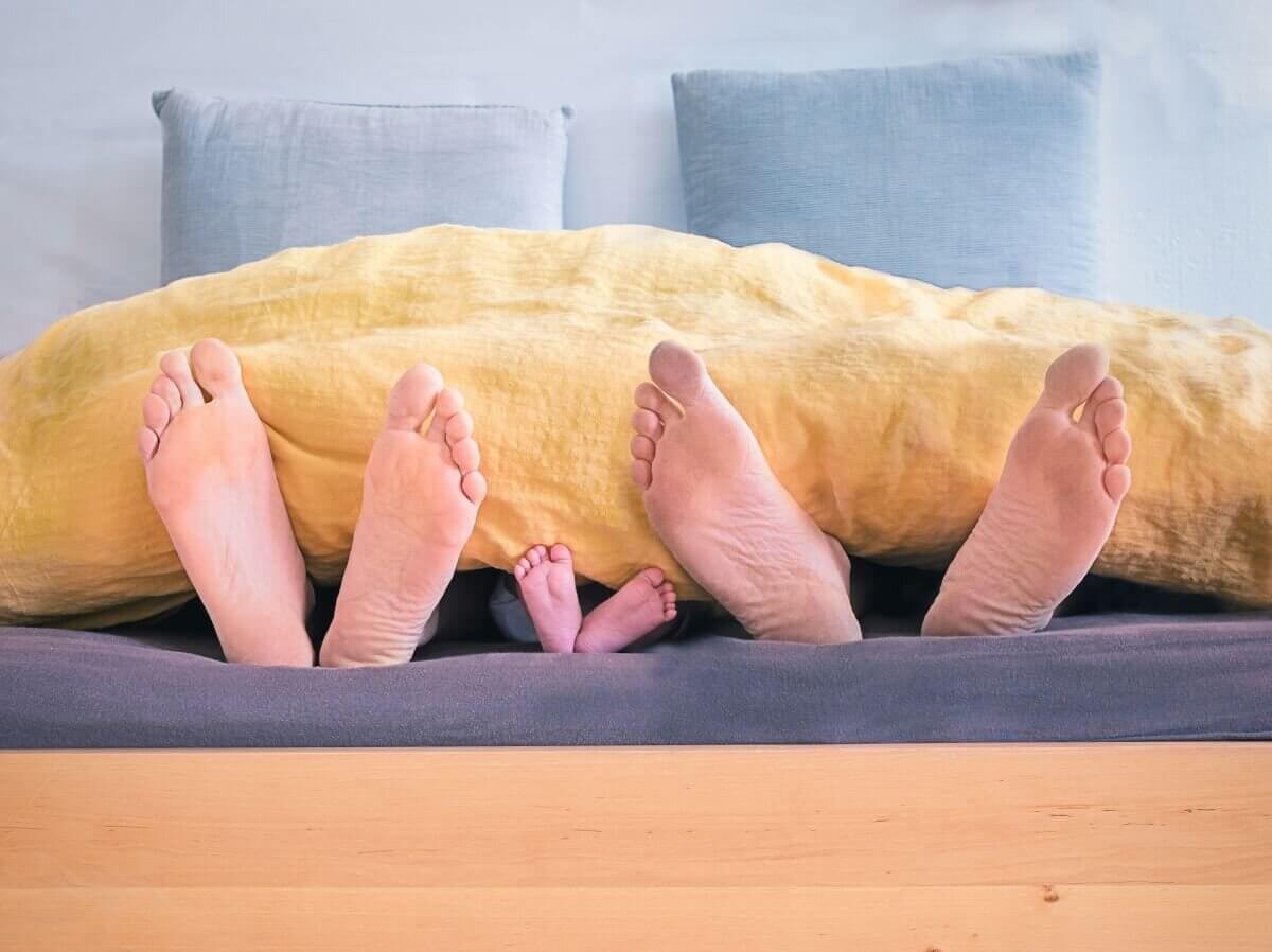 Parents' feet with child's feet sticking out of a bed