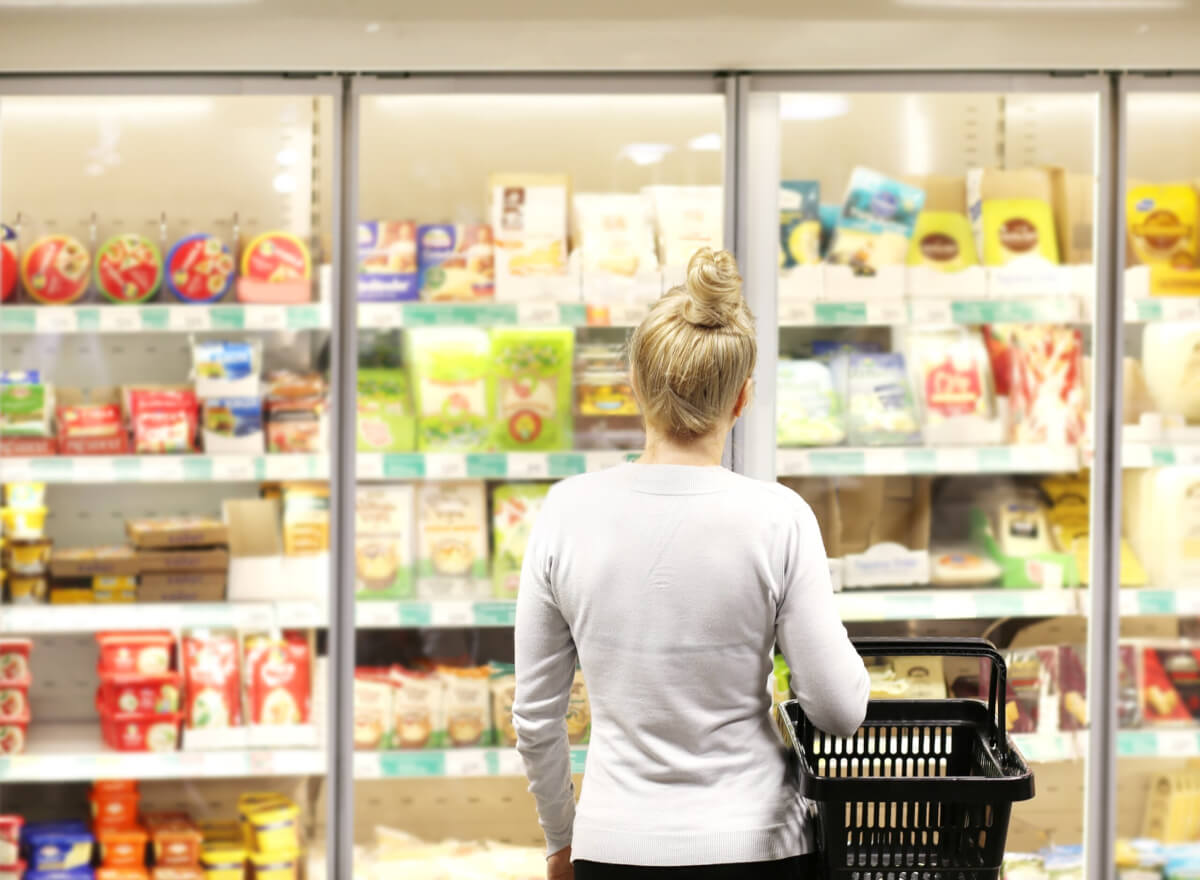 Woman choosing frozen food from a supermarket freezer, reading product information