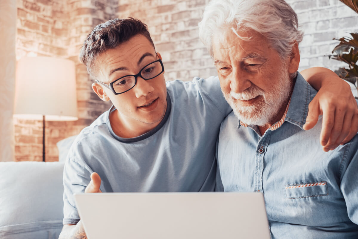 young man helping senior grandfather browse with laptop