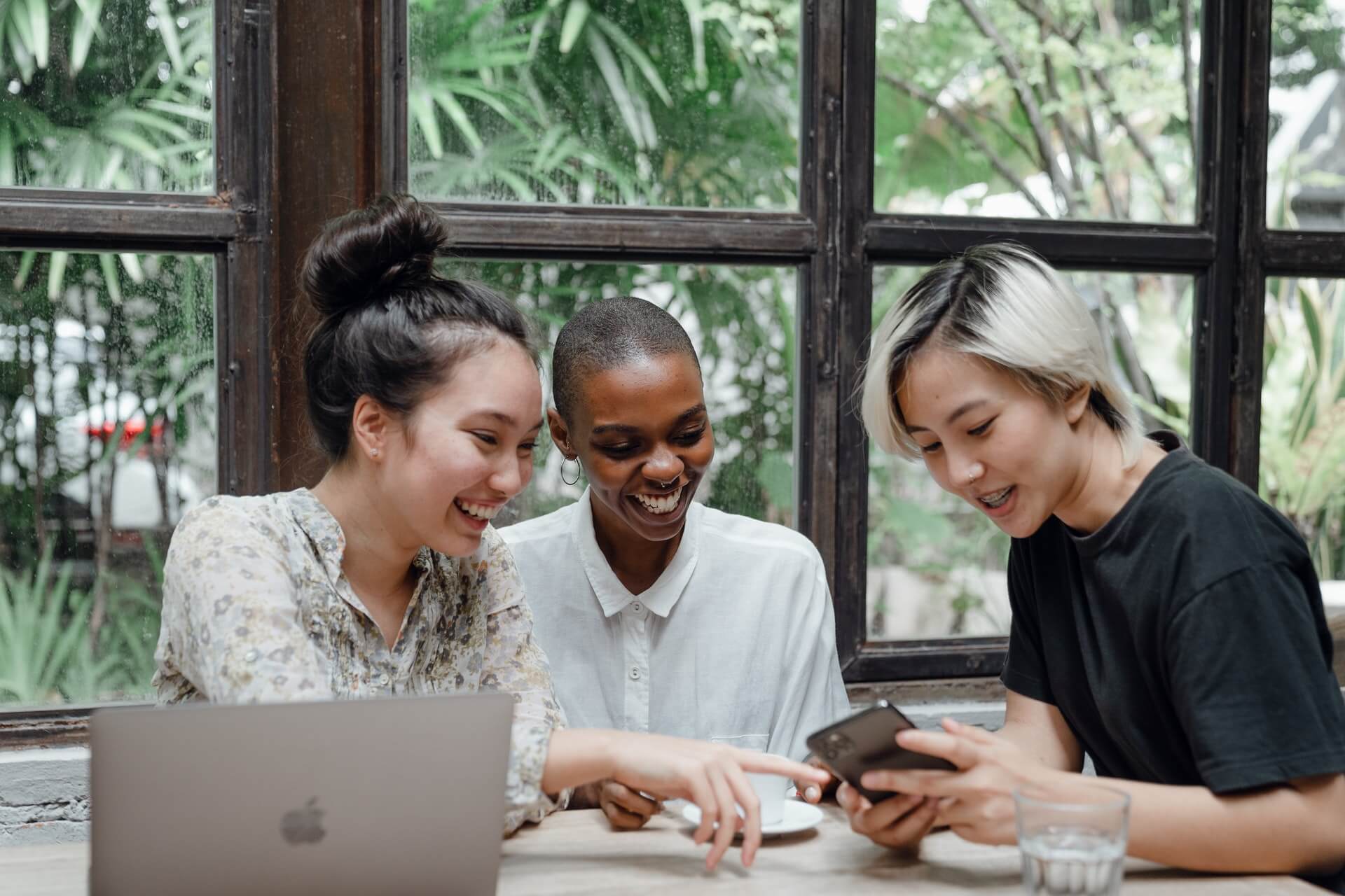 Friends laughing while looking at computer, phone during meeting