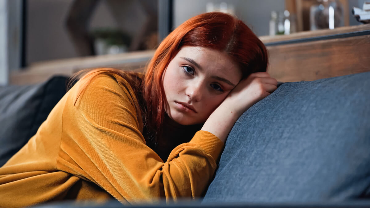 Sad teen girl laying on a couch alone