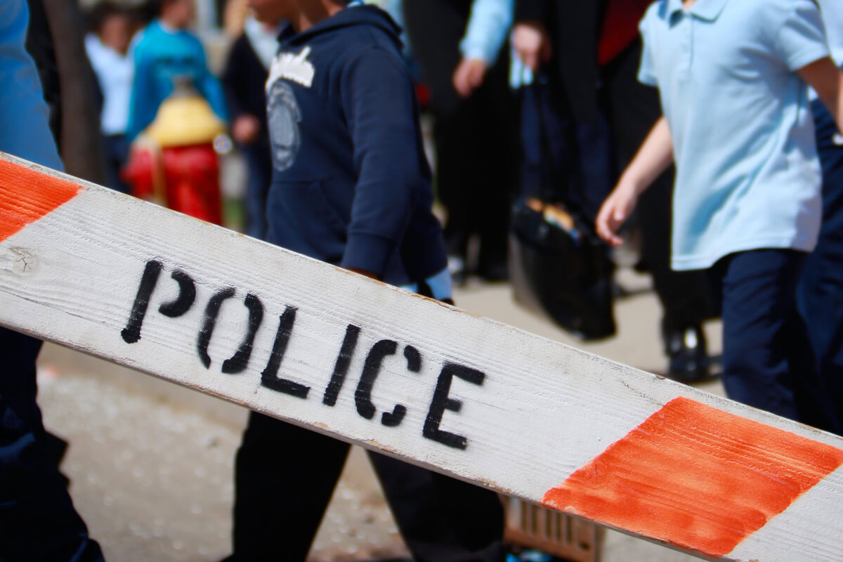 Police barricade with children in the background being evacuated.