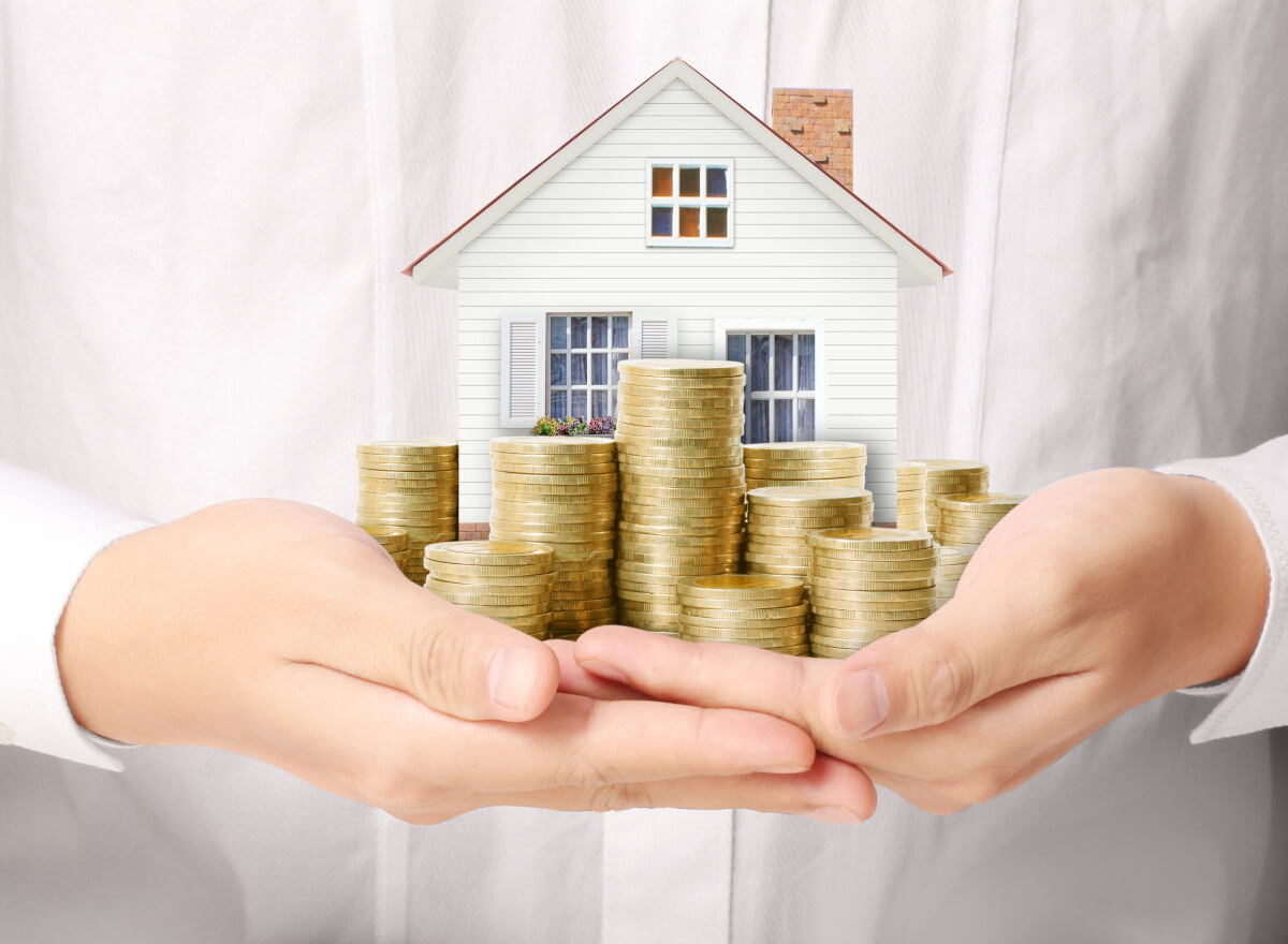 A woman holding a model home and a pile of coins