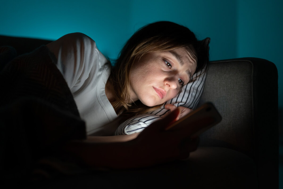 Sad woman in bed looking at smartphone